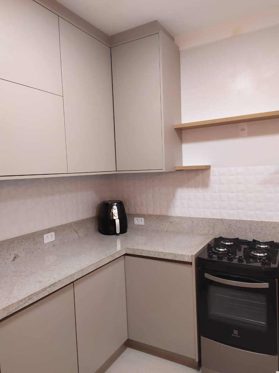 Cozinha compacta planejada em tons neutros com bancada em L, prateleiras e eletrodomésticos