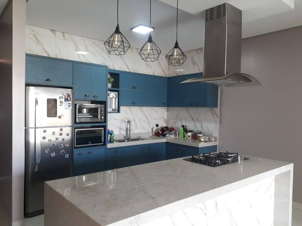 Cozinha planejada azul com ilha em pedra clara, armários sob medida, geladeira e coifa