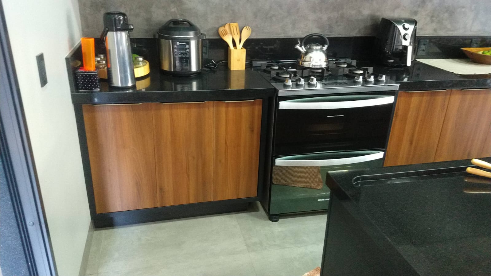 Cozinha planejada com armários superiores escuros, geladeira inox e bancada preta