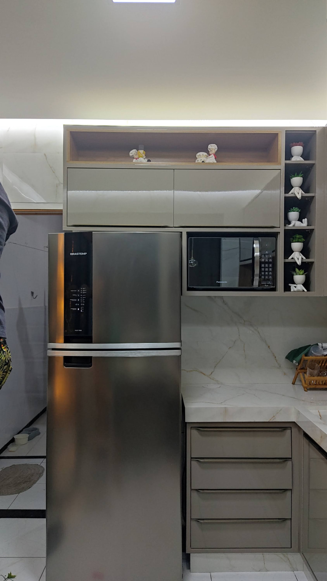 Cozinha planejada com armários superiores claros, geladeira inox e nichos iluminados