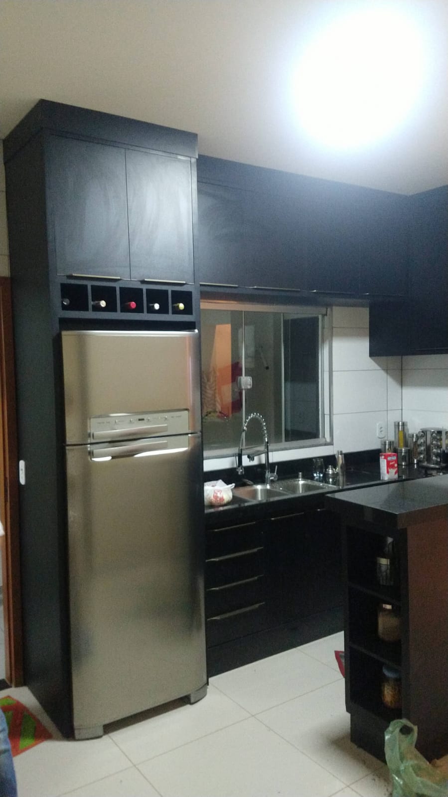 Cozinha planejada escura com armários superiores, geladeira inox e bancada preta