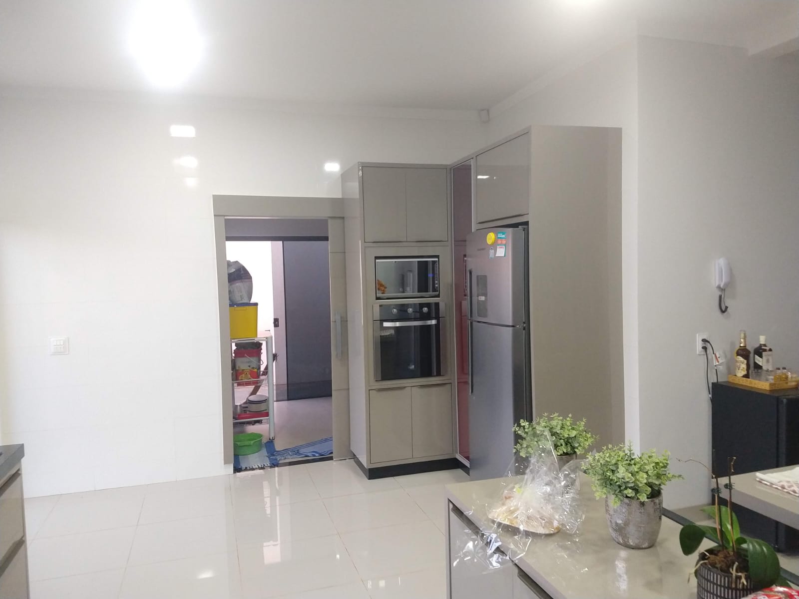 Cozinha planejada clara com armários em tom neutro, geladeira inox e torre de eletrodomésticos