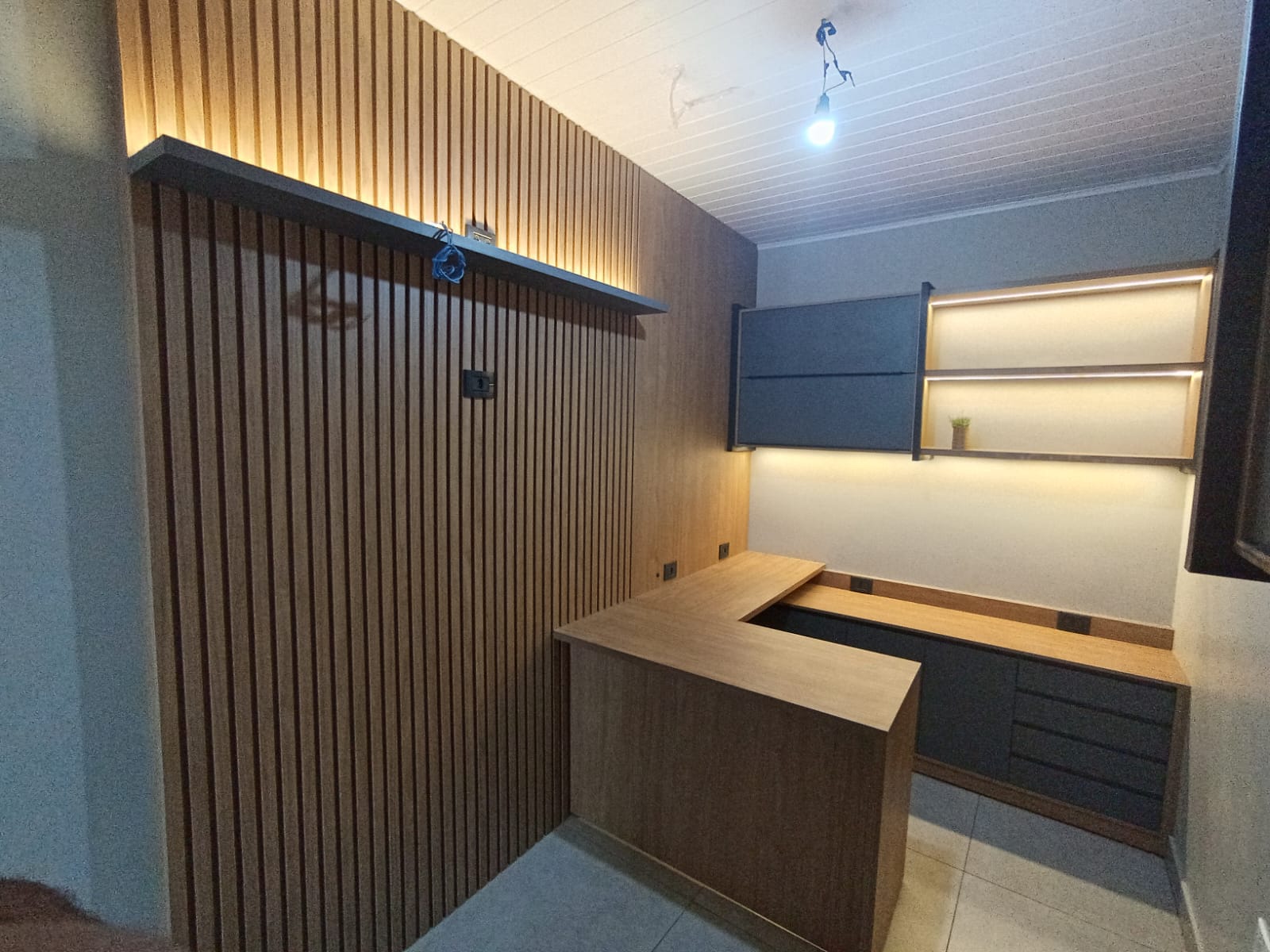 Home office completo com painel ripado, bancada em L, prateleiras com LED e marcenaria sob medida